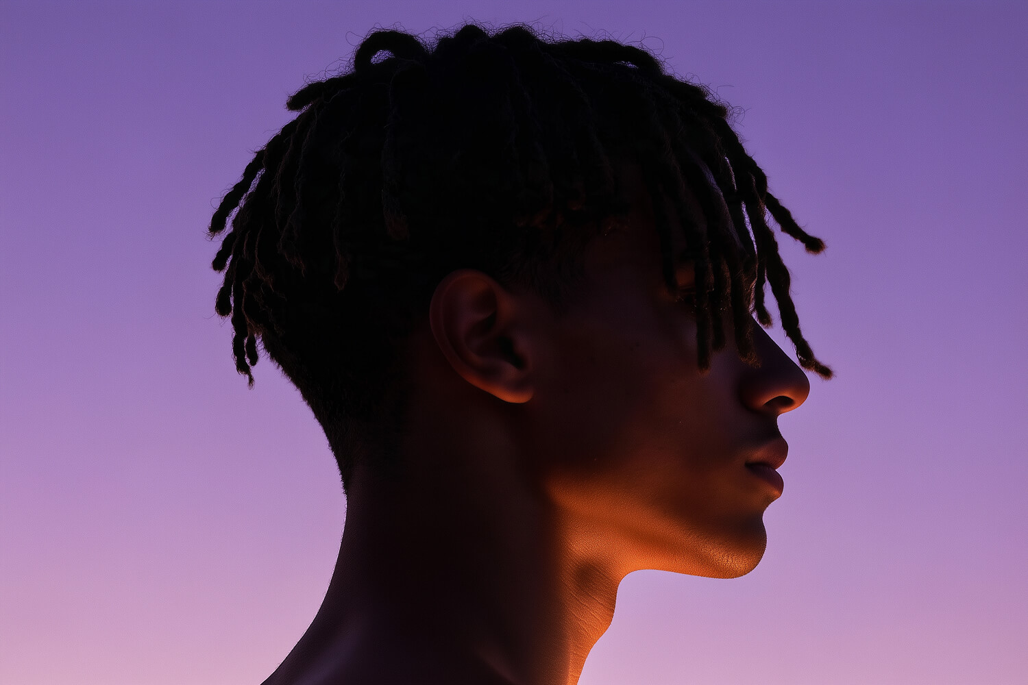 Profile of a man with twisted locs against a violet dusk sky