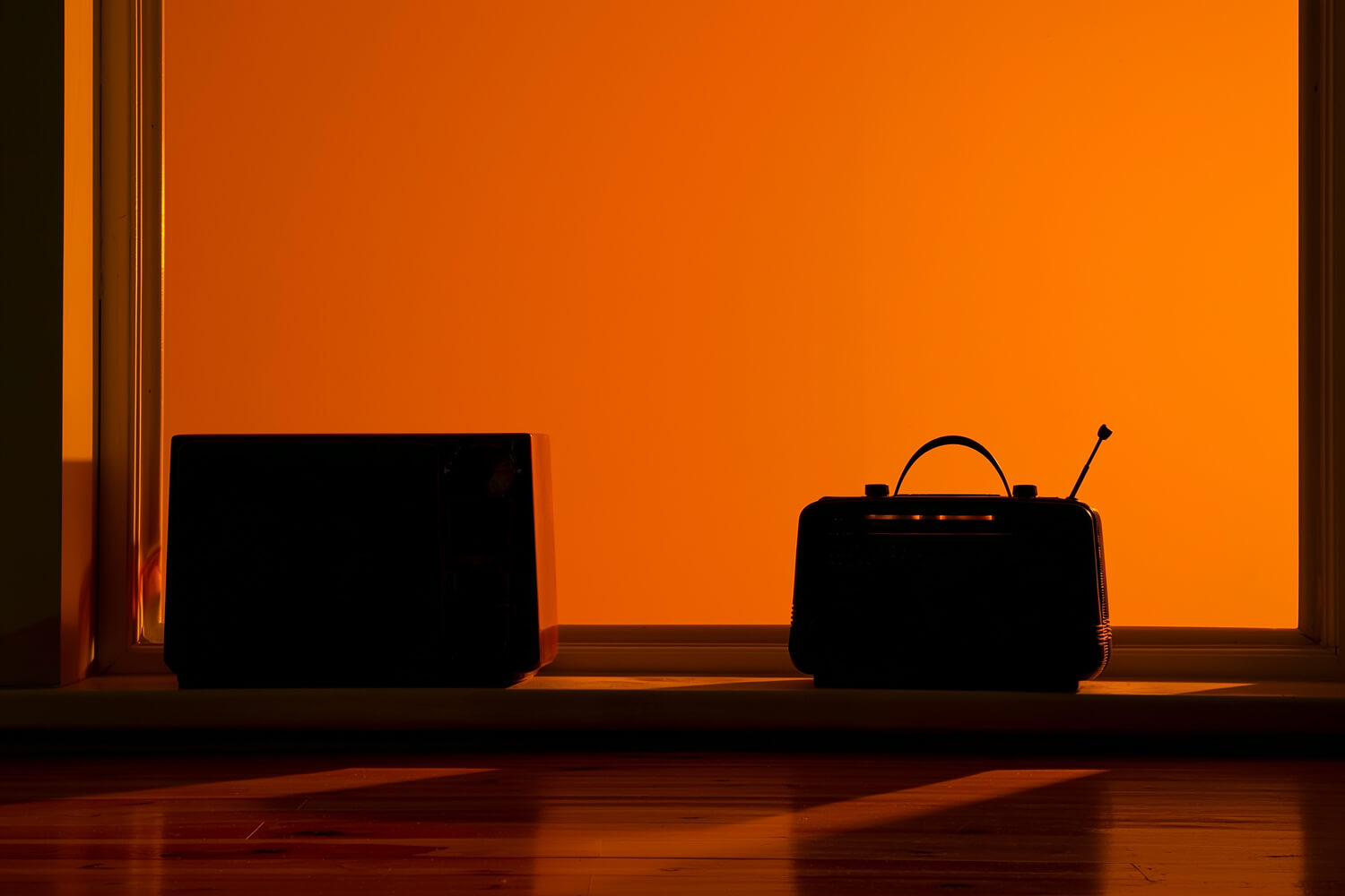 Silhouettes of a vintage radio and speaker on a windowsill against an orange glow