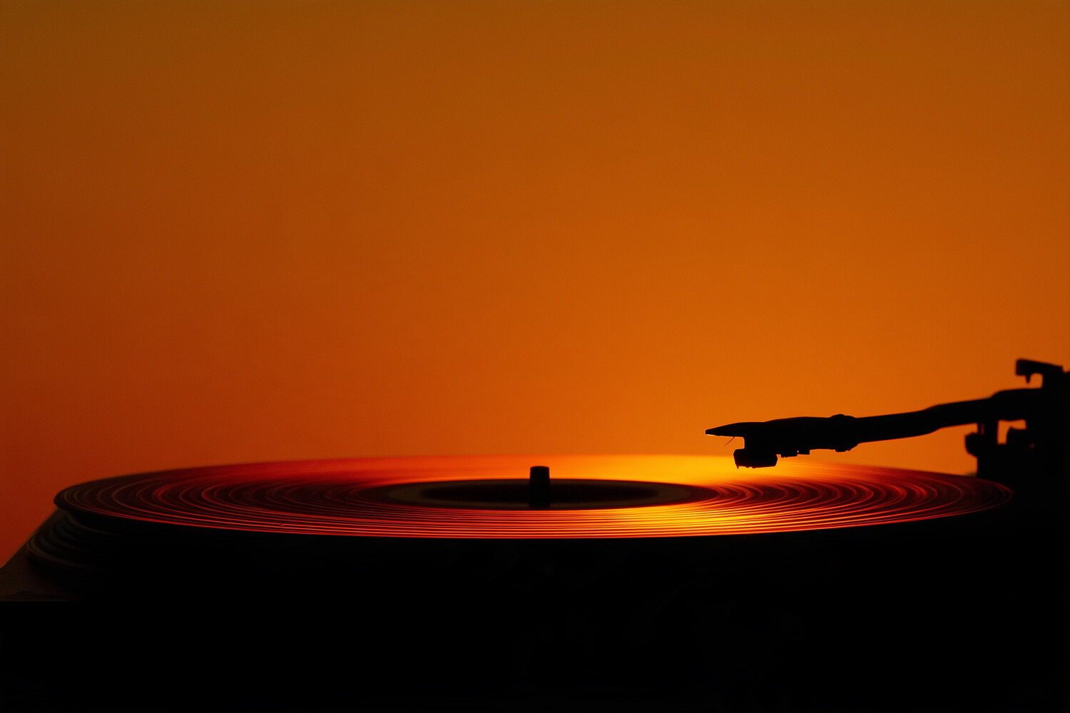 Turntable silhouetted against an amber sky, its record lit along the edge